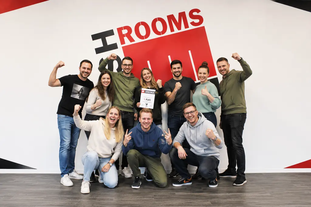 Elf Kolleginnen und Kollegen ballen die Fäuste, in der Mitte eine Urkunde für den ersten Platz